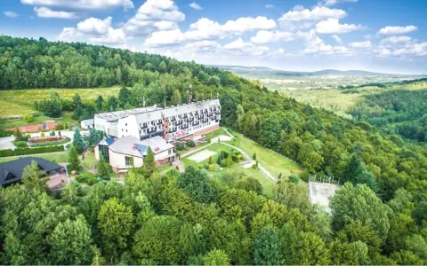 Hotel w otoczeniu zielonych lasów Gór Świętokrzyskich, blisko Kielc. Widok z lotu ptaka na budynki i krajobraz.