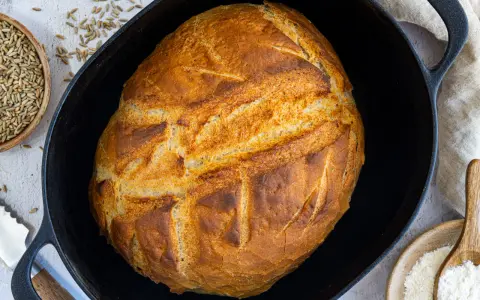 Ein goldbraunes Brot mit knuspriger Kruste liegt in einem Gusseisentopf. Dieses Brot kommt nicht aus dem Topf, sondern wurde darin gebacken.