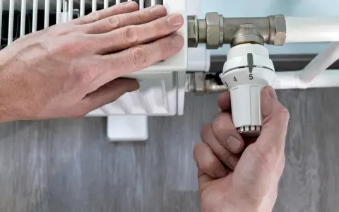Mano ajusta el termostato de un radiador. El radiador solo calienta la mitad derecha, indicando un posible problema.
