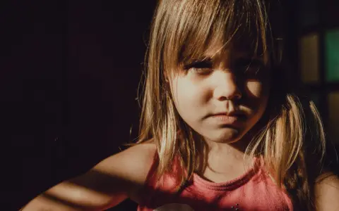 Niña con expresión seria, con luz de ventana en su rostro. A veces, mi hijo de 9 años se enoja por todo, pero hoy solo mira con intensidad.