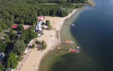 Skorzęcin jezioro z lotu ptaka: piaszczysta plaża, kolorowe rowery wodne, budynki i las.