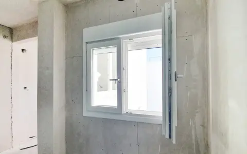 Instalar ventana PVC en obra gris. Ventana blanca de doble cristal con manilla plateada, lista para ser fijada.