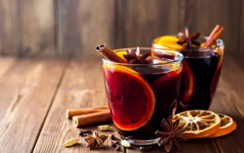 Dwa szklane kieliszki z grzanym winem, ozdobione plastrami pomarańczy, laskami cynamonu i anyżem. Idealne naczynia, w czym podawać grzane wino.