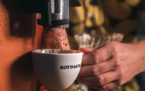 Mielona kawa spada do filiżanki z napisem "Kofimatik". Idealna baza do kawy z likierem kawowym Baileys.