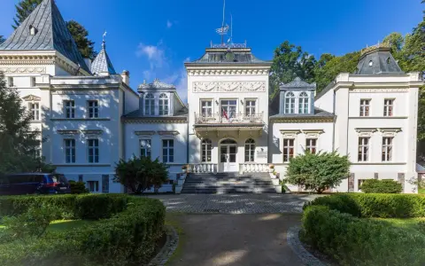 Elegancki pałac w Nosowie z wieżyczkami i ozdobnym balkonem, otoczony zielenią.