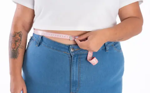 Persona plus size se mide la cintura con una cinta métrica rosa.