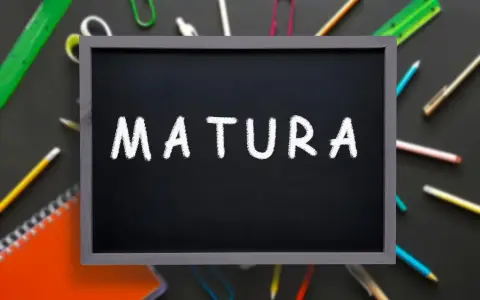 Czarna tablica z napisem "MATURA" kredą, otoczona przyborami szkolnymi. To symbol ważnego świadectwa dojrzałości.