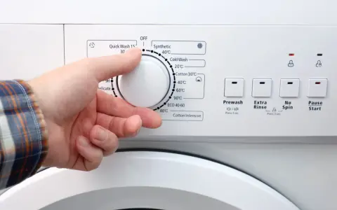 Dłoń ustawia pokrętło pralki. W ilu stopniach prac białe ubrania? Programy wskazują od 20°C do 90°C.