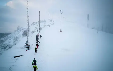 Deltagare i Hammarby Alpin Marathon kämpar sig uppför en snöig backe med skidstavar.