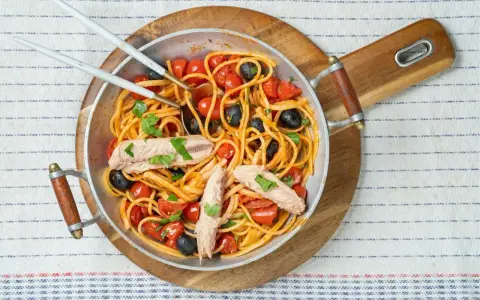 Pyszne spaghetti alla puttanesca z tuńczykiem, pomidorkami i czarnymi oliwkami w metalowej patelni, gotowe do podania.