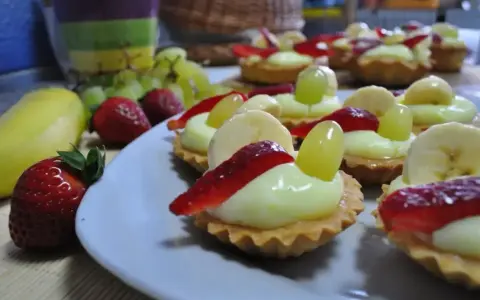 Pyszne babeczki z budyniem, udekorowane truskawkami, bananami i winogronami, wyglądają apetycznie.