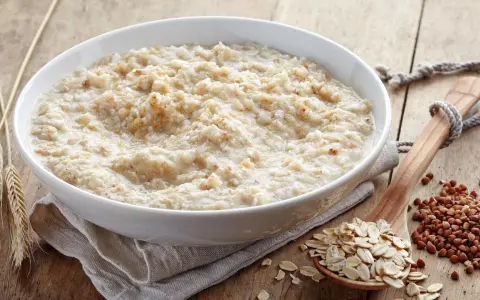 Schüssel mit Haferbrei, daneben Haferflocken und Buchweizen. Gute Haferkur Erfahrungen beginnen mit einem gesunden Frühstück.