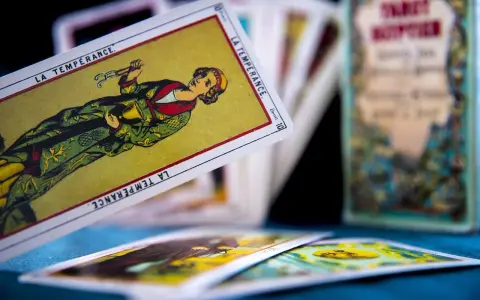 Rozłożone karty tarot 3 karty: "La Tempérance" w centrum, inne karty w tle i pudełko z napisem "Tarot".