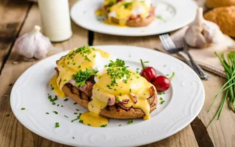 Huevos Benedictinos en plato blanco con salsa holandesa, perejil y chiles rojos.