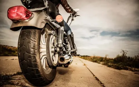 Osoba na motocyklu, widok z tyłu. Błyszczące chromy, skórzana kurtka i dżinsy. Droga prowadzi w dal, pod chmurami.