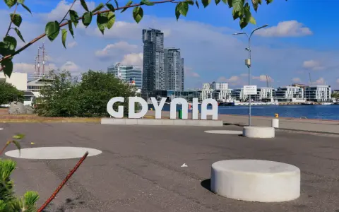 Napis GDYNIA na tle nowoczesnej architektury i żaglowca. Widok na port i budynki w Gdynia old town.