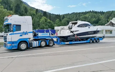 Ein LKW transportiert eine weiße Yacht auf einem Tieflader. Informieren Sie sich über bootstransport kosten für Ihre nächste Überführung.