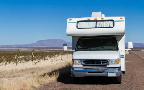 Weißer Freeway Camper steht am Straßenrand in karger Landschaft mit Bergen am Horizont.