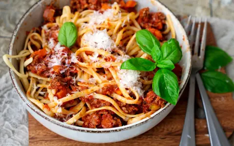 Eine Schüssel mit Linguine und einer herzhaften, **schnellen Bolognese**, garniert mit frischem Basilikum und Parmesan.