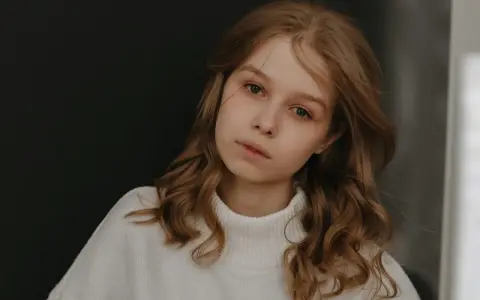 Młoda dziewczyna z burzą brązowych włosów, w białym golfie, zamyślona. Zastanawia się, jak przeprosić dziewczynę, by naprawić błąd.