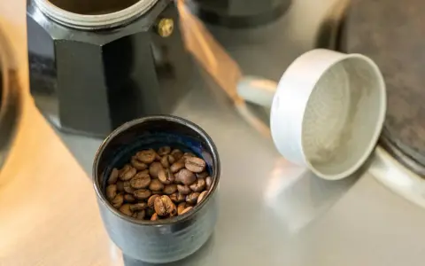 Kaffeebohnen in einer Schale neben einer Bialetti-Kaffeemaschine. Die Frage "bialetti wie viel kaffee" wird durch die Zubereitung beantwortet.