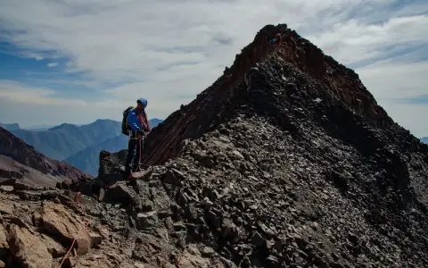 Alpinista na grani, zdobywający najwyższy szczyt Gruzji. W tle skaliste pasmo górskie i błękitne niebo.