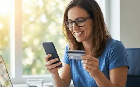 Mujer sonríe mientras usa su móvil y tarjeta para activar tarjeta BBVA.