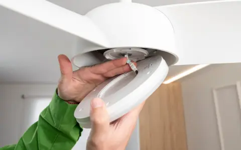Man installing a ceiling fan with light. Close-up of hands connecting wires to the light fixture.