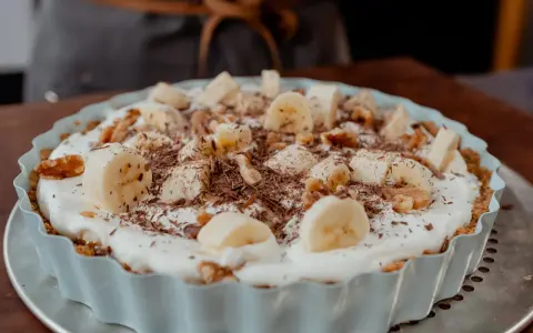 Tarte banane caramel onctueuse, garnie de rondelles de banane, noix et copeaux de chocolat. Un délice gourmand.