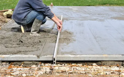 Un ouvrier ajuste le coffrage d'une dalle en béton frais avec une règle de maçon.