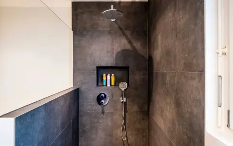 Ducha moderna con tabique de obra y muro de cristal. Incluye alcachofa de lluvia, grifería empotrada y nicho con botes de champú.