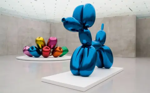 Un chien ballon bleu iconique de Jeff Koons, reflétant l'espace d'exposition. D'autres sculptures de ballons colorés sont visibles en arrière-plan.