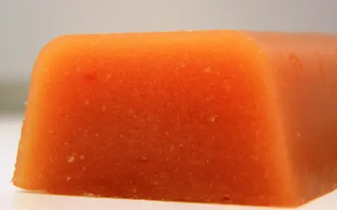 Bloque naranja de carne de membrillo, con textura granulada y bordes redondeados.