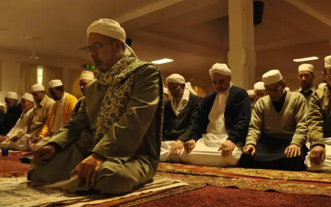 Männer in weißen Turbanten und traditioneller Kleidung knien auf Gebetsteppichen und verrichten das Taraweeh-Gebet.