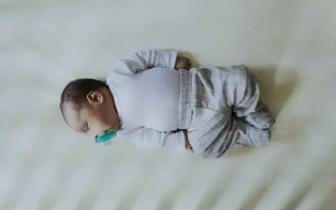Śpiące dziecko z niebieskim smoczkiem, ułożone na boku. Może to być oznaka kręcz szyi, ale maluch wygląda na spokojnego.