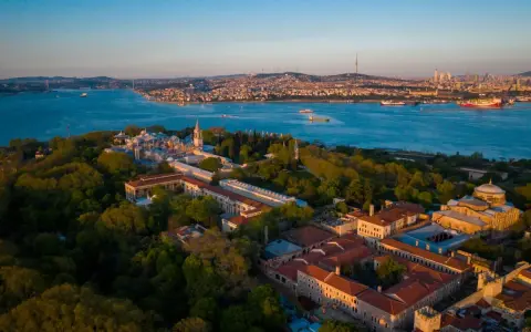 Aerial view of the Topkapi Palast complex, nestled amongst lush greenery, with the Bosphorus Strait and Istanbul skyline in the background.