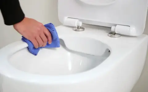 Main propre avec un chiffon bleu, nettoyant le bord d'un wc avec bride ou sans bride.