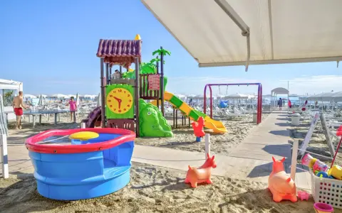 Area giochi su sabbia con scivolo, altalena e giochi d'acqua, un vero lido per bambini.