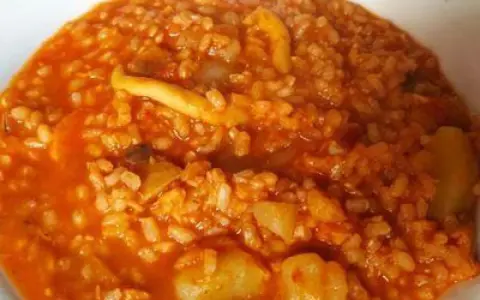 Arroz caldoso con trozos de marisco y verduras en salsa rojiza.