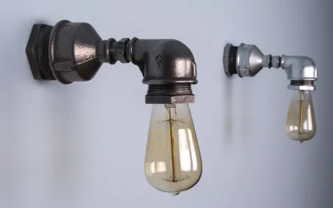 Dwie industrialne lampy z rurek, jedna większa, ciemniejsza, druga mniejsza, jaśniejsza, obie z żarówkami Edisona.