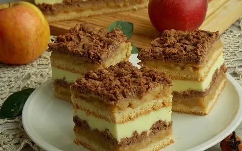Pyszna szarlotka z budyniem, z jabłkami i kruszonką, podana na talerzu obok jabłek.