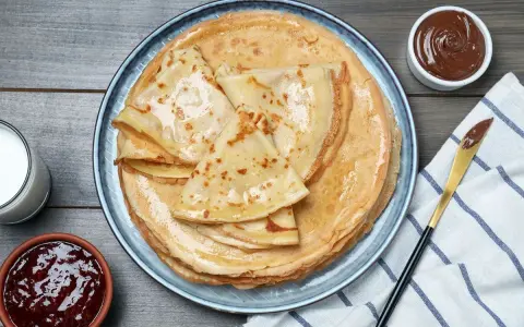 Pile de crêpes dorées, parfaites pour une recette pâte à crêpes. Accompagnées de confiture, pâte à tartiner et verre de lait.