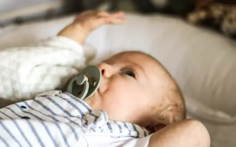 Uroczy noworodek z niebieskimi oczami i smoczkiem. Sprawdzam temperaturę noworodka na czole, by upewnić się, że jest mu komfortowo.