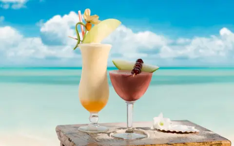 Dwa egzotyczne drinki, jeden kremowy, drugi owocowy, z Malibu na tropikalnej plaży. Idealne na wakacje.