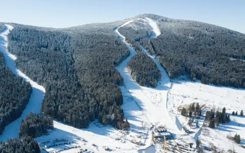 Widok z lotu ptaka na czarna góra resort, ośrodek górski z trasami narciarskimi wśród ośnieżonych lasów i budynkami u podnóża góry.