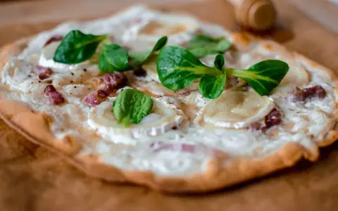 Tarte flambée alsacienne garnie de lardons, fromage de chèvre et jeunes pousses.