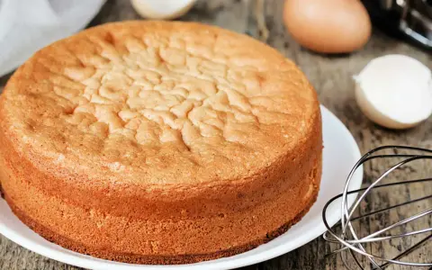 Perfekter Biskuitboden: Ein goldbrauner Kuchen, bereit für Ihr nächstes biskuitboden rezept. Eier und Schneebesen deuten auf die Zubereitung hin.