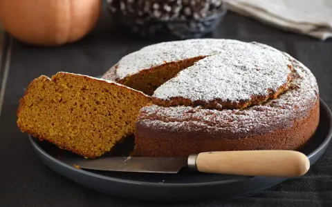 Bizcocho de calabaza esponjoso y dorado, espolvoreado con azúcar glas. Una rebanada muestra su interior húmedo y aromático.