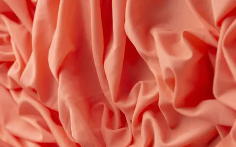 Tessuto arancione con pieghe morbide. Il materiale acrilico, cos'è? Una fibra sintetica versatile e resistente, ideale per abbigliamento e tessuti d'arredo.