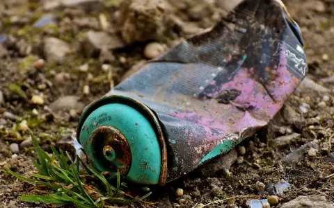 Lata de aerosol aplastada y oxidada en el suelo, un ejemplo de las causas de la contaminación.